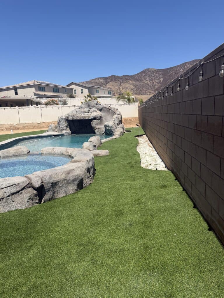 Residential backyard with pool, rock waterfall, and mountain backdrop.